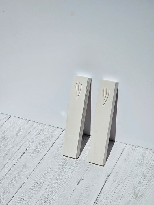 Two stone-look mezuzah cases with engraved Shin standing against a wall, minimalist handmade Judaica by Gifts LA