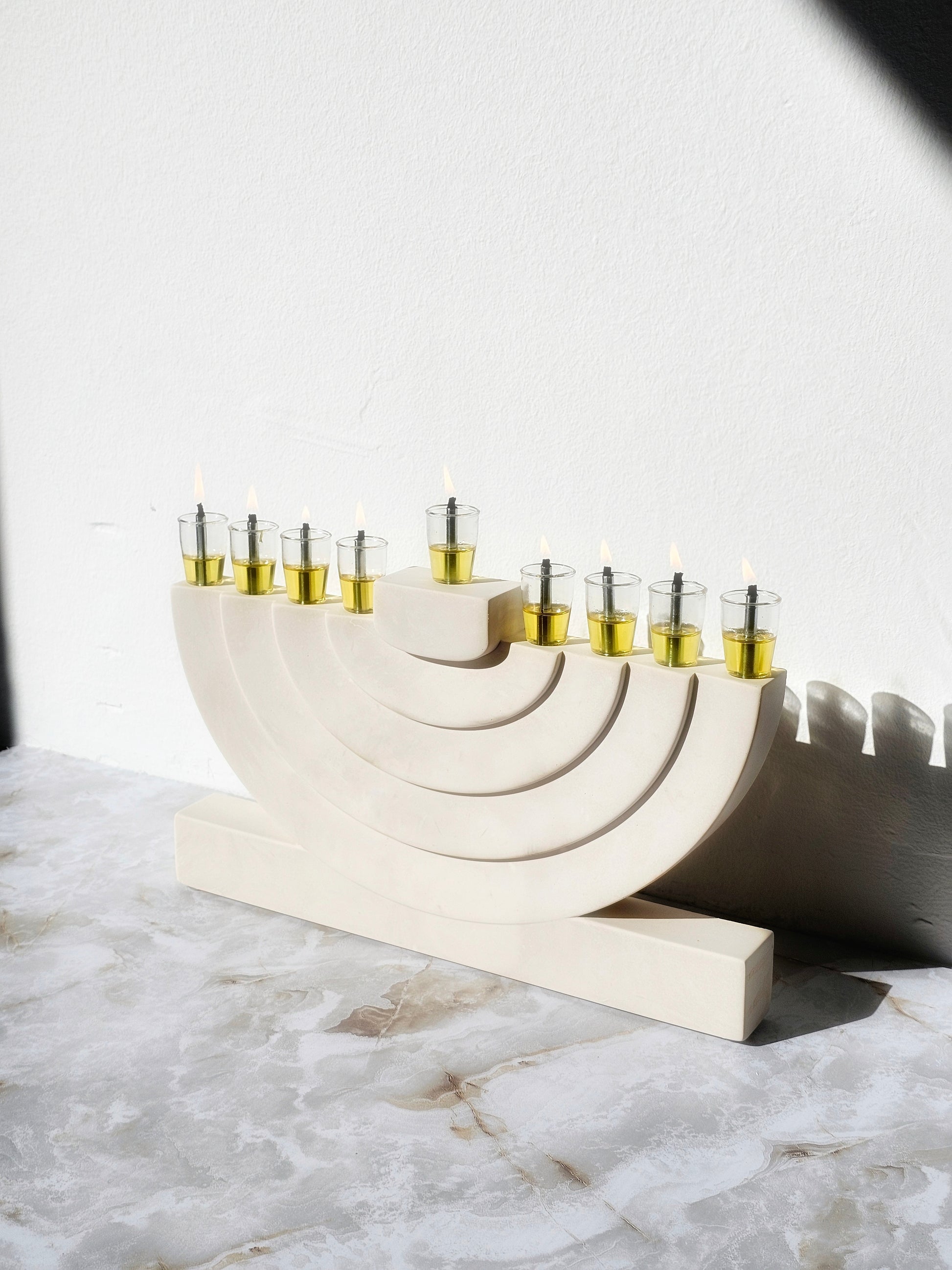 Handcrafted luxury stone-look menorah with layered arch form and glass oil cups, made for a modern warm elegant Hanukkah home